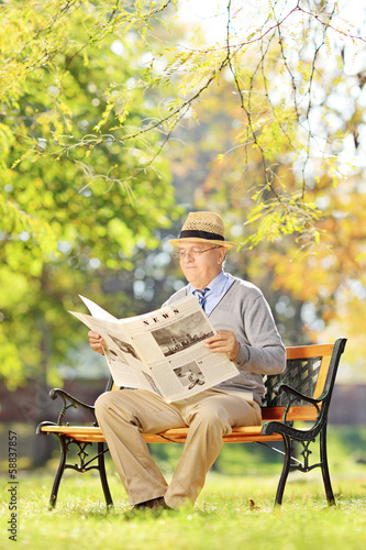 Photo: Senior gentleman with hat sitting on bench and reading a newspap Senior gentleman with hat sitting on bench and reading a newspap