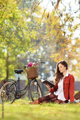 Photo: Young beautiful female reading a novel in a park Young beautiful female reading a novel in a park