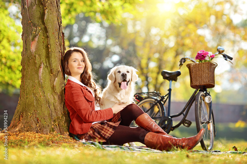 Photo: Young female sitting on a grass with her dog in a park Young female sitting on a grass with her dog in a park