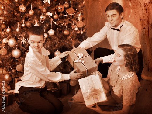 Photo: Family with children receiving gifts under Christmas tree. Family with children receiving gifts under Christmas tree.