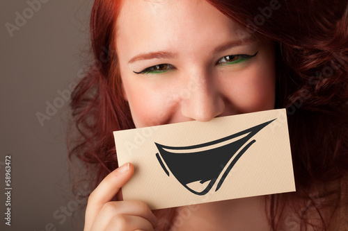 Photo: Happy cute girl holding paper with funny smiley drawing Happy cute girl holding paper with funny smiley drawing