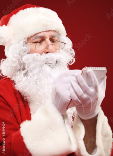 Photo: Christmas portrait of Santa Claus writing a list isolated on red Christmas portrait of Santa Claus writing a list isolated on red