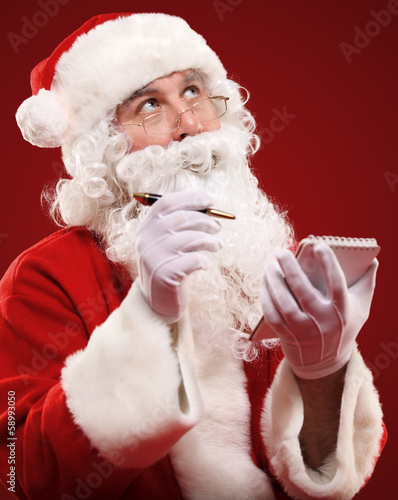 Photo: Christmas portrait of Santa Claus writing a list isolated on red Christmas portrait of Santa Claus writing a list isolated on red
