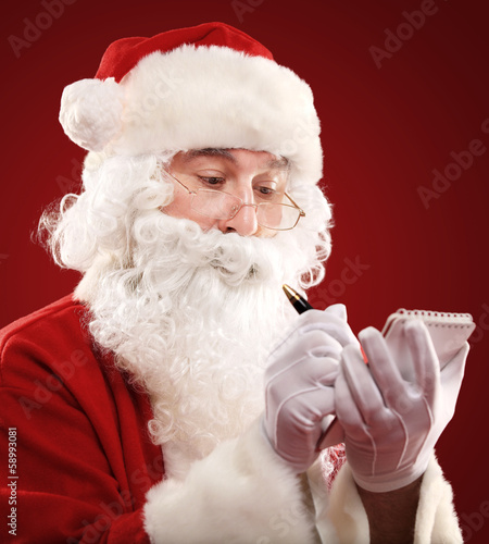 Photo: Christmas portrait of Santa Claus writing a list isolated on red Christmas portrait of Santa Claus writing a list isolated on red