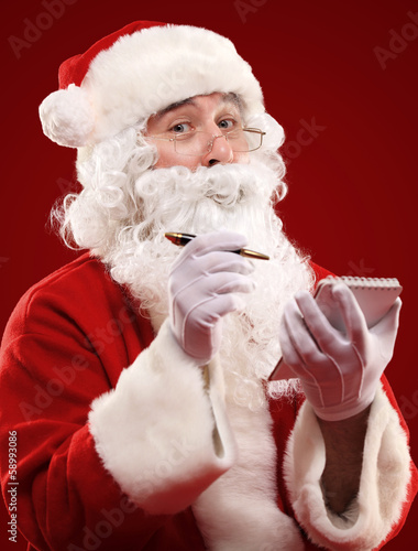 Photo: Christmas portrait of Santa Claus writing a list isolated on red Christmas portrait of Santa Claus writing a list isolated on red