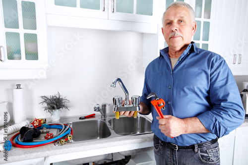 Photo: Plumber in kitchen with a wrench. Plumber in kitchen with a wrench.