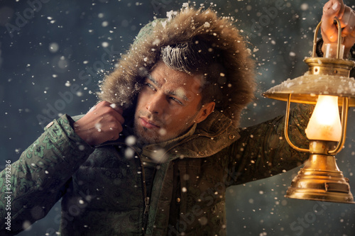 Photo: Brutal man walking under snowstorm at night lighting his way wit Brutal man walking under snowstorm at night lighting his way wit