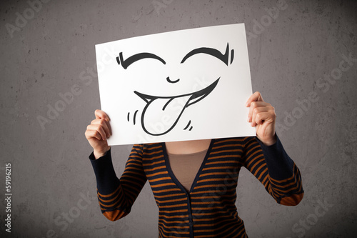 Photo: Woman holding a paper with cute smiley face on it in front of he Woman holding a paper with cute smiley face on it in front of he