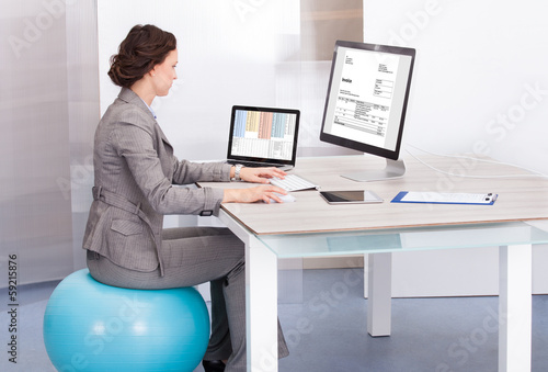 Photo: Woman Sitting On Pilates Ball Using Computer Woman Sitting On Pilates Ball Using Computer