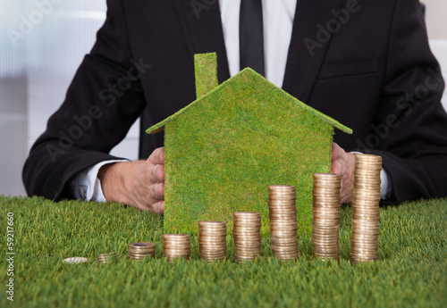 Photo: Businessman With Stack Of Coins And Eco Friendly House Businessman With Stack Of Coins And Eco Friendly House