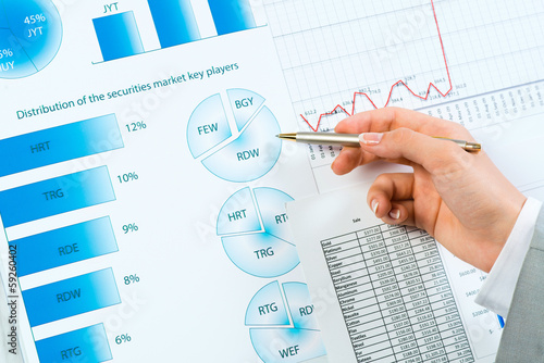 Photo: female hand pointing pen on financial charts female hand pointing pen on financial charts