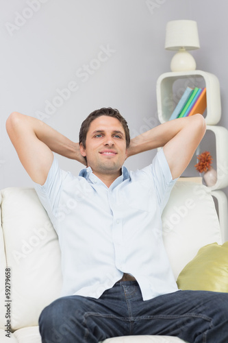 Photo: Thoughtful man sitting with hands behind head in the living room Thoughtful man sitting with hands behind head in the living room
