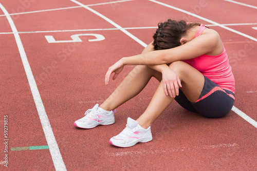 Photo: Tensed sporty woman sitting on the running track Tensed sporty woman sitting on the running track