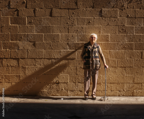 Photo: Old senior woman standing brick wall background Old senior woman standing brick wall background