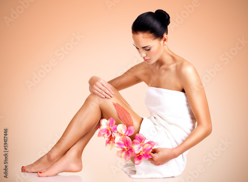 Photo: Beautiful young woman with flowers using a scrub. Beautiful young woman with flowers using a scrub.
