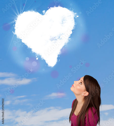 Photo: Cute girl looking at white heart cloud on blue sky Cute girl looking at white heart cloud on blue sky