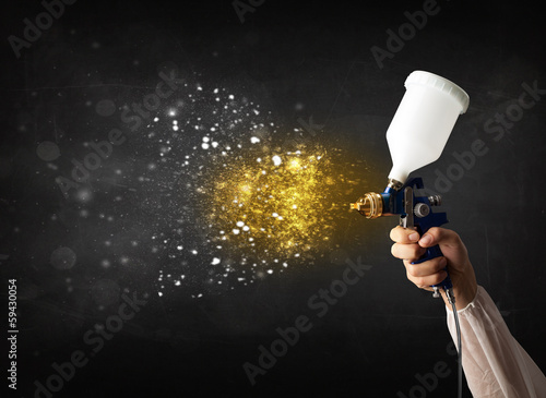 Photo: Worker with airbrush painting with glowing golden paint Worker with airbrush painting with glowing golden paint