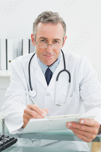 Photo: Portrait of a doctor writing a report at office Portrait of a doctor writing a report at office
