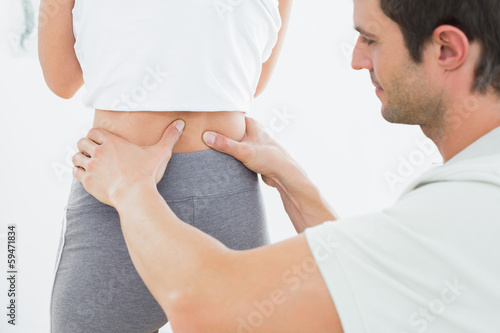 Photo: Mid section of a physiotherapist examining woman's back Mid section of a physiotherapist examining woman's back