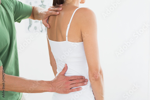 Photo: Physiotherapist examining woman's back in medical office Physiotherapist examining woman's back in medical office