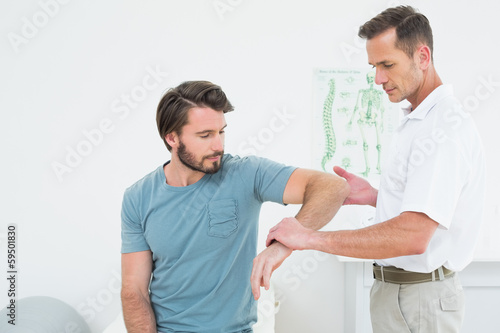 Photo: Male physiotherapist examining a young man's arm Male physiotherapist examining a young man's arm