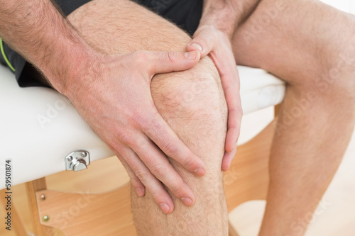 Photo: Mid section of a man with his hands on a painful knee Mid section of a man with his hands on a painful knee