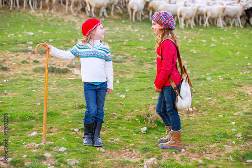 Photo: Kid girl shepherdess sisters happy with flock of sheep and stick Kid girl shepherdess sisters happy with flock of sheep and stick