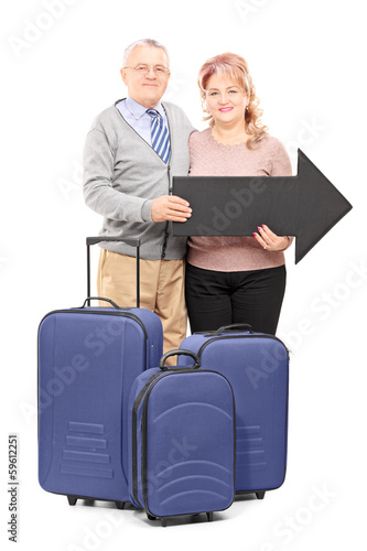 Photo: Smiling mature tourists holding a big black arrow and travel bag Smiling mature tourists holding a big black arrow and travel bag