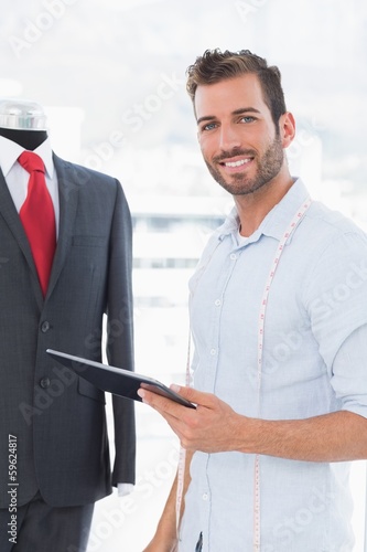 Photo: Fashion designer with digital tablet by suit on dummy Fashion designer with digital tablet by suit on dummy