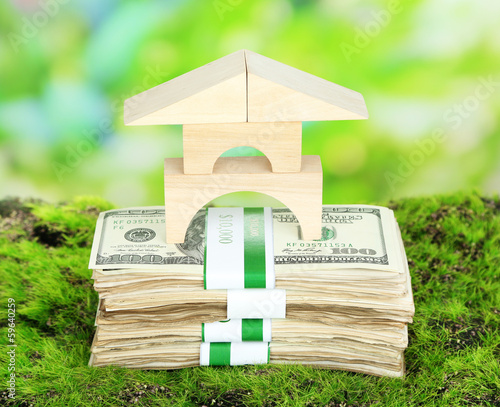 Photo: Wooden house on packs of dollars on grass on natural background Wooden house on packs of dollars on grass on natural background