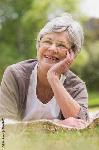 Photo: Smiling senior woman lying at park Smiling senior woman lying at park