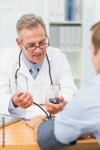 Photo: Smiling doctor taking his patients blood pressure Smiling doctor taking his patients blood pressure
