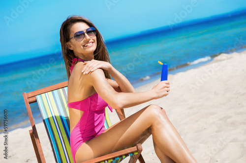 Photo: A young woman in a swimsuit adding suntan on the beach A young woman in a swimsuit adding suntan on the beach