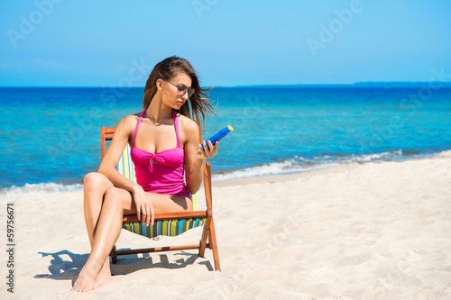 Photo: A young woman in a swimsuit adding suntan on the beach A young woman in a swimsuit adding suntan on the beach