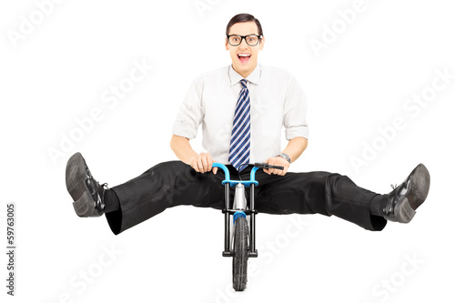 Photo: Excited young businessman with tie riding a small bicycle Excited young businessman with tie riding a small bicycle