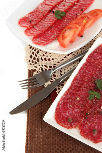 Photo: Tasty salami on plates on napkin isolated on white Tasty salami on plates on napkin isolated on white