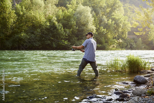 Photo: Fisherman standing near river and holding fishing rod Fisherman standing near river and holding fishing rod