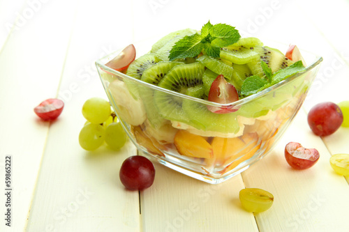 Photo: Tasty fruit salad in glass bowl, on white wooden table Tasty fruit salad in glass bowl, on white wooden table