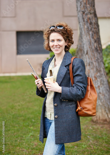 Photo: Female redhead student carrying notebook and coffee to go Female redhead student carrying notebook and coffee to go