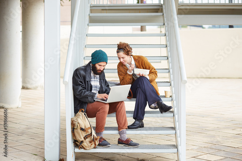 Photo: Hipster couple using computer and eating lunch outdoors Hipster couple using computer and eating lunch outdoors