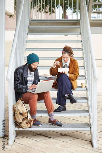 Photo: Hipster couple using computer and eating lunch outdoors Hipster couple using computer and eating lunch outdoors