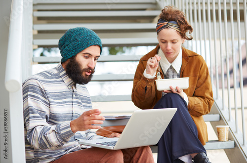 Photo: Hipster couple using computer and eating lunch outdoors Hipster couple using computer and eating lunch outdoors