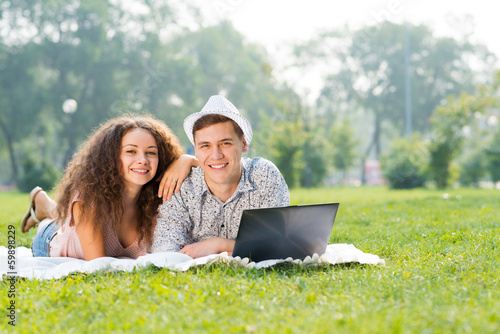 Photo: couple lying together in a park with laptop couple lying together in a park with laptop
