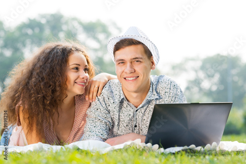 Photo: couple lying together in a park with laptop couple lying together in a park with laptop