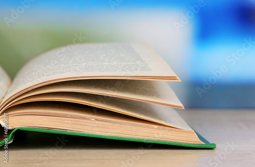 Photo: Opened book on wooden table on bright background Opened book on wooden table on bright background