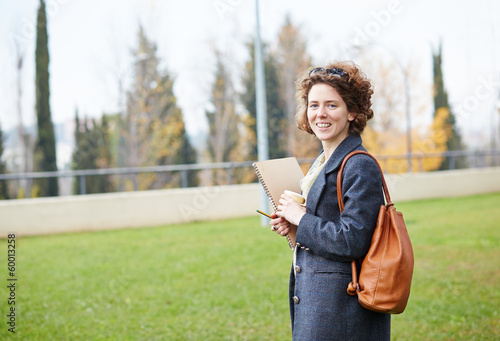 Photo: Female redhead student carrying notebook and coffee to go Female redhead student carrying notebook and coffee to go