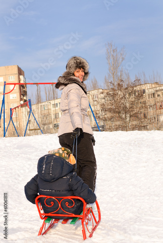 Photo: Mother pulling a toboggan with her child in snow Mother pulling a toboggan with her child in snow
