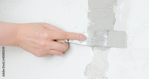 Photo: Female hand repairs wall with spackling paste Female hand repairs wall with spackling paste