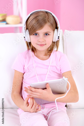 Photo: Little girl listening music sitting on sofa in room Little girl listening music sitting on sofa in room