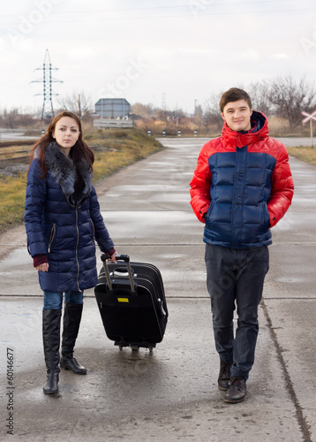 Photo: Young couple walking on the road with a suitcase Young couple walking on the road with a suitcase